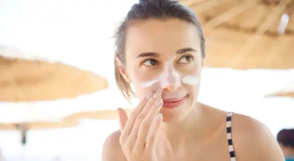 Frau trägt Sonnencreme auf ihr Gesicht auf, um Sonnenbrand zu vermeiden.