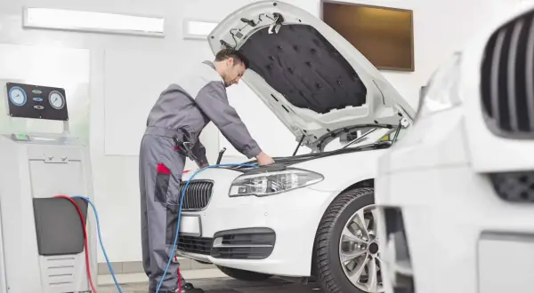 Mechanik sprawdza silnik białego BMW. Zastanawiasz się, ile teraz kosztuje przegląd samochodu?