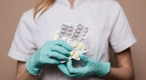 Farmaceuta w rękawiczkach trzyma kilka opakowań tabletek.