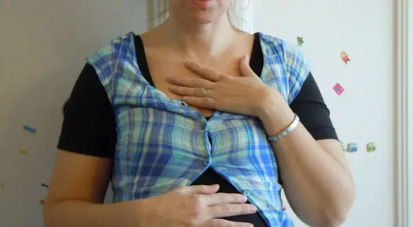 En kvinna med en rutig skjorta över en svart topp, håller händerna över magen. Hon ser ut att vara **rennie gravid**.