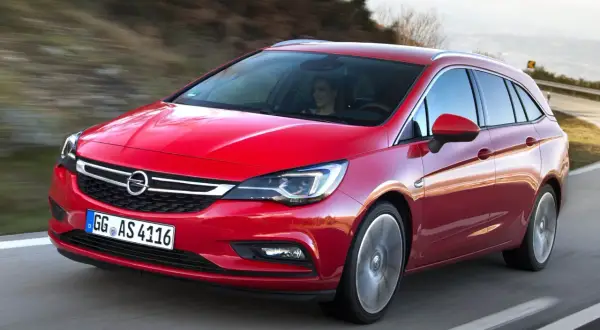 Röd Opel Astra kombi 2016 körs på en väg. En kvinna syns bakom ratten. Kanske ett problem med bilen?