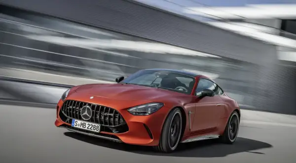 Pomarańczowy Mercedes-AMG GT 63 S pędzi po drodze, za nim rozmyte tło nowoczesnej architektury.