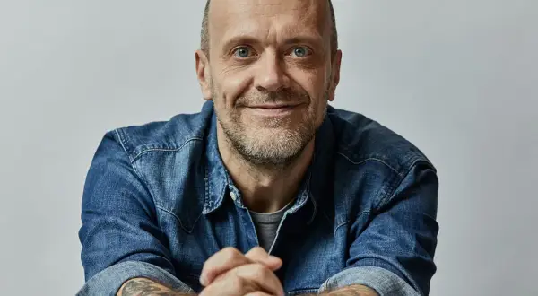 Uomo con barba corta, occhi azzurri, indossa una camicia di jeans. Le sue mani sono intrecciate, eccoti testo.