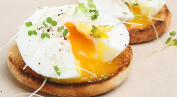 Dos deliciosos huevos poche sobre tostadas inglesas, adornados con brotes verdes y pimienta. La yema dorada fluye, invitando a un bocado perfecto.