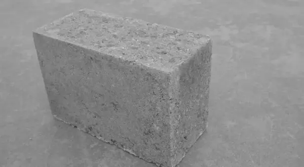 Szary bloczek betonowy na szarym tle. Jego wymiary są standardowe, idealny do budowy.