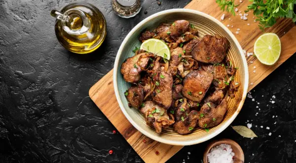 Un piatto invitante di fegatini di pollo saltati con cipolle, guarnito con fette di lime e prezzemolo fresco. Accanto, olio d'oliva, sale grosso e pepe.