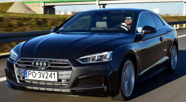 Czarny Audi A5 na drodze. Kierowca w okularach przeciwsłonecznych. Wiele osób chwali audi a5 opinie.