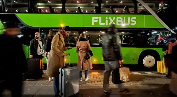 Ludzie z bagażem czekają na zielonego Flixbusa.