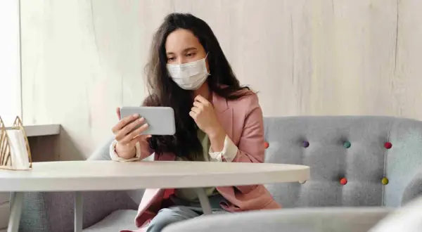Donna con mascherina guarda il telefono, forse per informarsi sulla situazione, mostrando una certa paura dei virus.