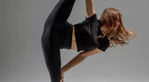 Une danseuse en tenue noire exécute un grand écart impressionnant, démontrant souplesse et grâce.