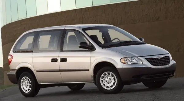 Srebrny Chrysler Voyager, gotowy na każdą podróż, zaparkowany przed budynkiem z ceglaną fasadą.