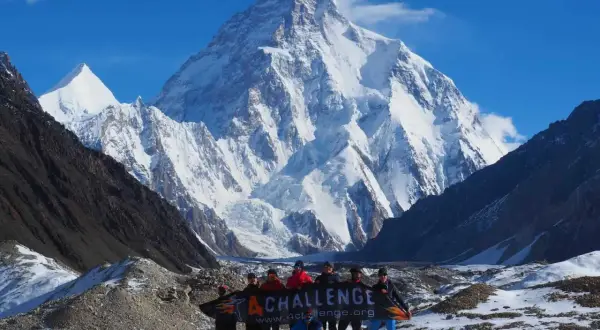 Grupa ludzi z banerem "4 CHALLENGE" na tle szerokiego, ośnieżonego szczytu.