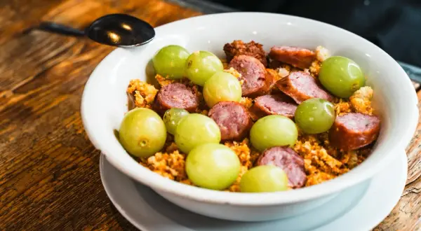 Un plato con uvas verdes, chorizo en rodajas y migas crujientes, un sabor que recuerda a el tubo zaragoza.