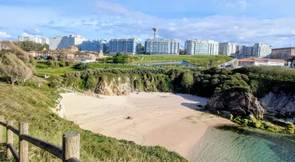 Playa en el parque de bens, con arena dorada, acantilados verdes y edificios modernos al fondo.