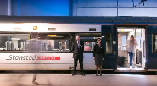 Pociąg Stansted Express na stacji. Pracownicy obsługi i pasażerowie wsiadają i wysiadają. Szybki transport z lotniska do centrum Londynu.