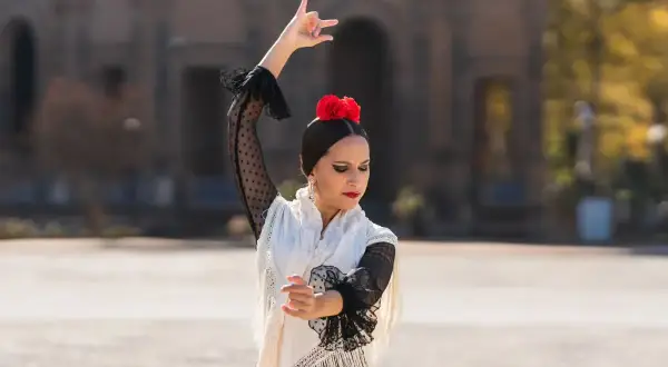 Bailarina de flamenco con un vestido blanco y negro, flor roja en el pelo, moviendo sus brazos al ritmo rumba.