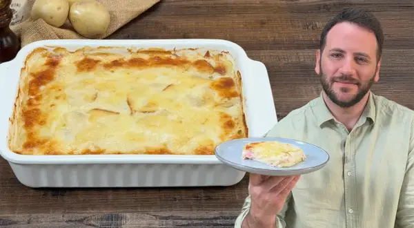 Un uomo sorride mostrando una porzione di parmigiana di patate appena sfornata, dorata e filante.
