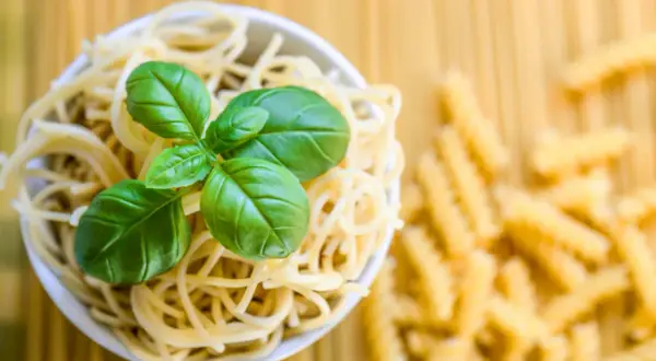 Miseczka spaghetti z bazylią, obok rozsypane fusilli. To klasyczne danie, gdzie co to jest semolina z pszenicy durum, stanowi podstawę.
