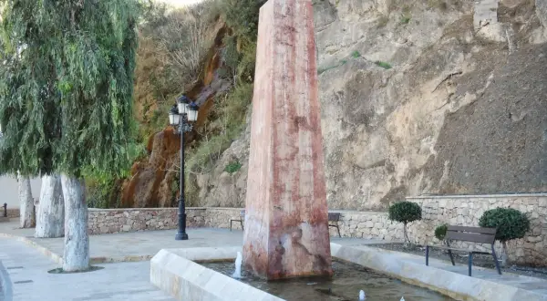 Obelisco en fuente con cascada alhama de almeria al fondo. Árboles y bancos invitan al descanso.
