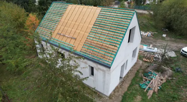 Dom w budowie, widoczne etapy budowy domu: ściany z bloczków, przygotowany dach pod pokrycie.