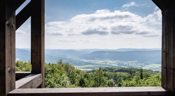 Widok z wieży widokowej na górę Cergową. Rozległa panorama Beskidu Niskiego, zielone lasy i pola, błękitne niebo z chmurami.