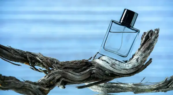 Szklana butelka perfum na dryfującym drewnie, w tle błękitna woda. Czy to zapach ambra co to?