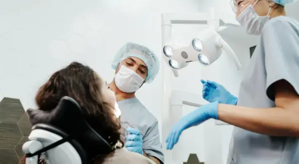 Dentysta i asystentka przygotowują się do zabiegu, kiedy leczenie kanałowe jest konieczne. Pacjentka siedzi na fotelu dentystycznym.