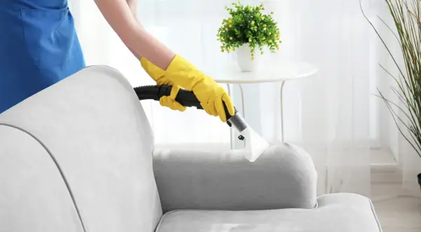 Person mit gelben Handschuhen reinigt Polstergarnitur mit einem Dampfreiniger.