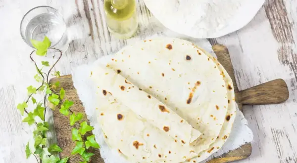 Domowy tortilla przepis: świeżo upieczone placki, mąka, olej i woda na drewnianej desce.