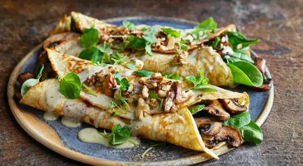 Herzhafte Pfannkuchen gefüllt mit Pilzen, garniert mit Nüssen und frischen Kräutern, übergossen mit cremiger Sauce.