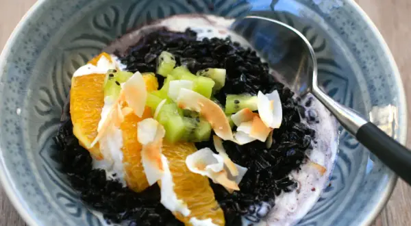 Schwarzer Reis mit Kokosmilch, garniert mit Orangenstücken, Kiwi und Kokoschips. Ein köstliches Dessert.