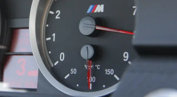 Wskaźnik pokazuje temperaturę oleju w silniku, która wynosi około 100°C. Obok znajduje się obrotomierz.