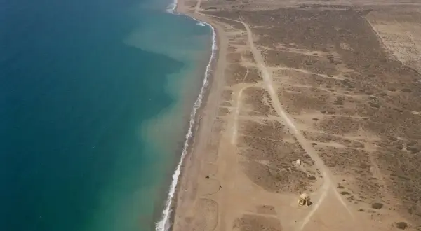 Vista aérea de la playa Torregarcia, con el mar turquesa a la izquierda y la costa arenosa con vegetación escasa y construcciones a la derecha.