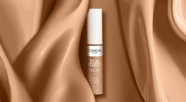 Un correcteur jaune L'Oréal True Match, présenté sur un fond satiné couleur peau.