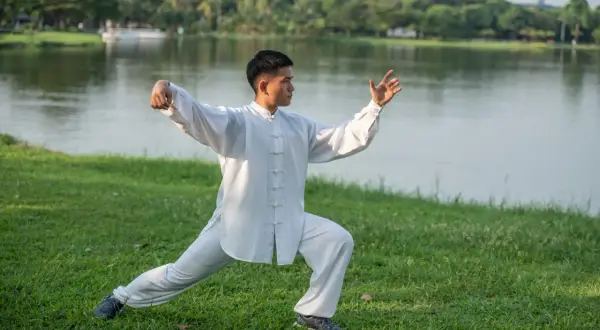Mężczyzna w białym stroju ćwiczy tai chi co to za sztuka walki, harmonijnie poruszając się nad jeziorem.