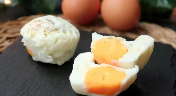 Huevos cocidos en microondas, uno entero y otro partido mostrando la yema naranja. Dos huevos enteros al fondo.