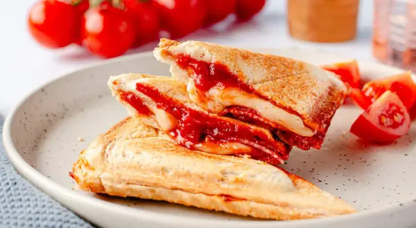 Herzhafte Sandwichmaker Rezepte: goldbraune Sandwiches mit geschmolzenem Käse und Tomatensoße, serviert mit frischen Tomaten.