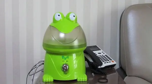 Zielony nawilżacz powietrza dla niemowlaka w kształcie żaby, obok telefonu.