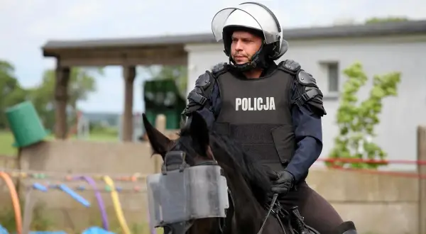 Policjant w pełnym rynsztunku, na koniu z osłoną na pysk, gotowy do akcji. Konie policyjne to ważny element służby.