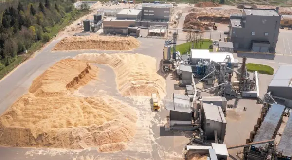 Vue aérienne d'une usine de transformation du bois avec d'énormes tas de sciure. Le prix de la sciure de bois à la tonne est un facteur clé pour cette industrie.