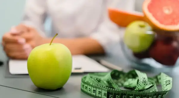 Zielone jabłko, miarka i owoce na stole. Wizyta u dietetyka, wsparcie Novo Nordisk w dbaniu o zdrowie.