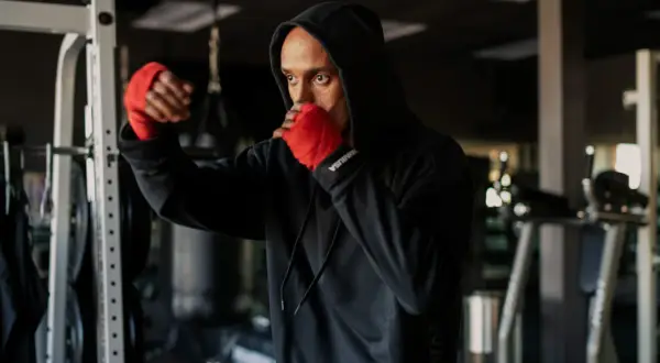 A man in a black hoodie with red hand wraps practices shadow boxing, his intense gaze reflecting the mental discipline of the sport.
