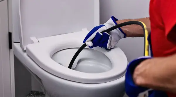 Ręka w rękawicy wprowadza spiralę do białej muszli klozetowej, by udrożnić zapchaną toaletę.