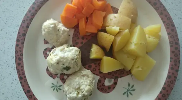 Na talerzu ułożone są delikatne pulpety dla niemowlaka, obok nich kawałki gotowanych ziemniaków i marchewki.