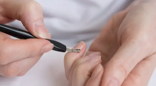 Dłonie podczas zabiegu japońskiego manicure. Narzędzie do usuwania skórek delikatnie pracuje przy paznokciu.