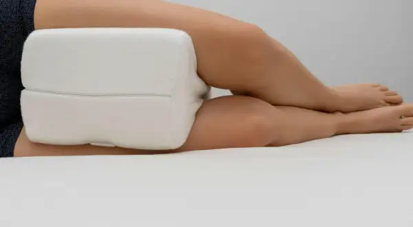 En person sover med ryggskott, med en vit kudde mellan knäna för stöd.