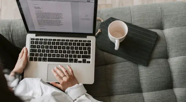 Person som arbetar med e-learning på en laptop i soffan, med en kaffekopp bredvid.