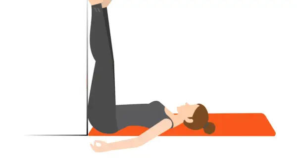 En kvinna stretchar rygg efter gym genom att ligga på en matta med benen uppåt mot en vägg.