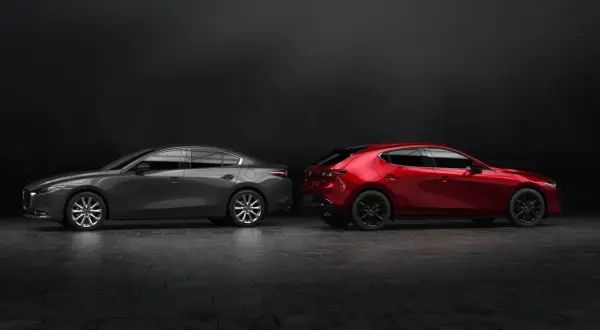 Szary sedan Mazda 3 i czerwony hatchback stoją obok siebie na ciemnym tle.