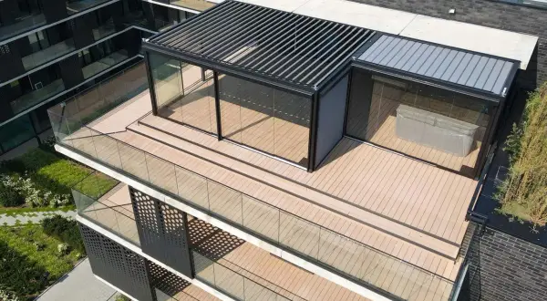Nowoczesny taras na dachu z przeszklonym pawilonem i pergolą. Drewniana podłoga i szklane balustrady tworzą elegancką przestrzeń.
